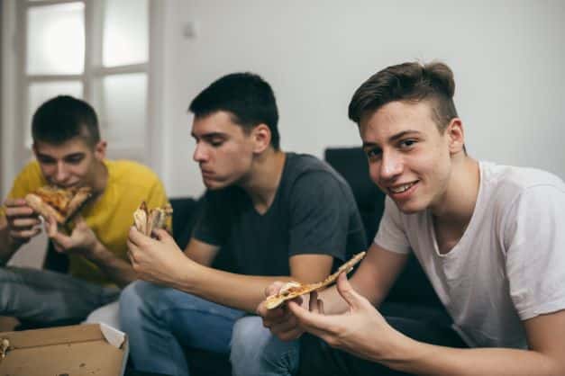 teen boy eating pizza with friends