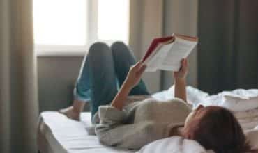 teen girl reading inspirational book on bed