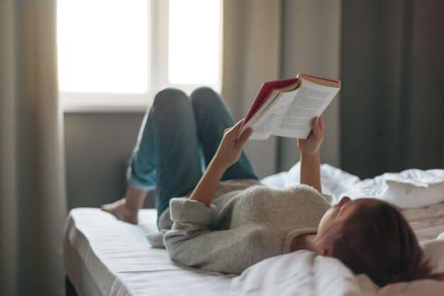 teen girl reading inspirational book on bed